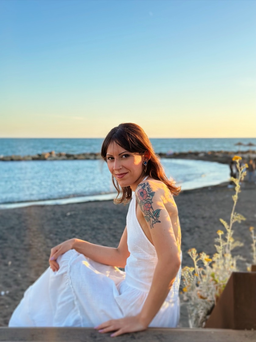 Jessica Milani seduta su una panca di legno in riva al mare, al tramonto.
